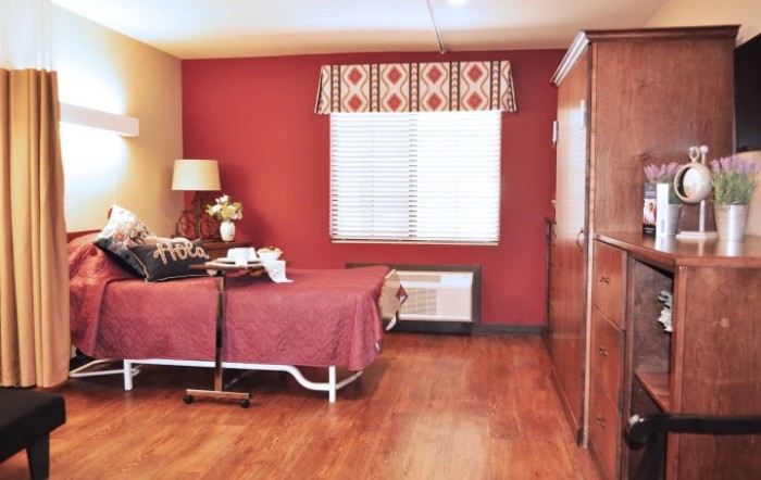 A cozy bedroom with red walls, a bed, wardrobe, and a lamp near the window.