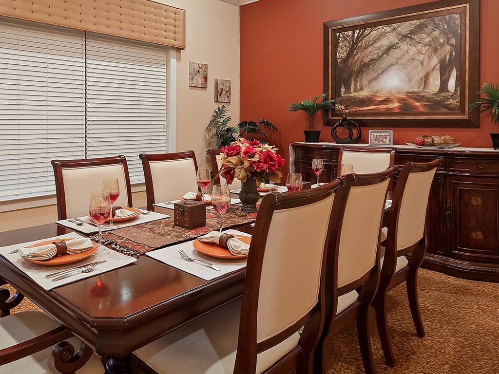 A well-decorated dining room featuring a polished wooden table set for a meal, surrounded by elegant chairs and accented with flowers and artwork.