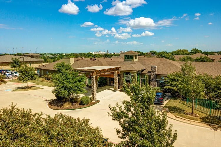 Aerial view of a modern building surrounded by lush greenery and a bright blue sky.