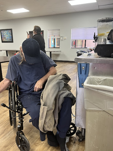 A person seated in a wheelchair, dressed casually, in what appears to be a medical facility.