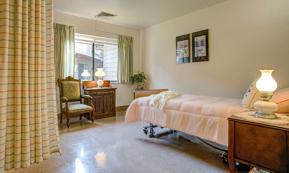 A cozy room with a hospital bed, armchair, and a window view.