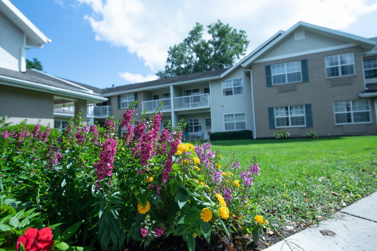 A sunny view of a well-maintained apartment complex with colorful flowers and lush green grass.