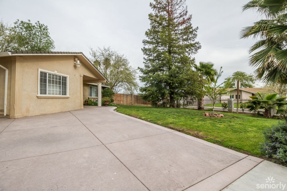 A suburban house with a concrete driveway and a grassy yard surrounded by trees.