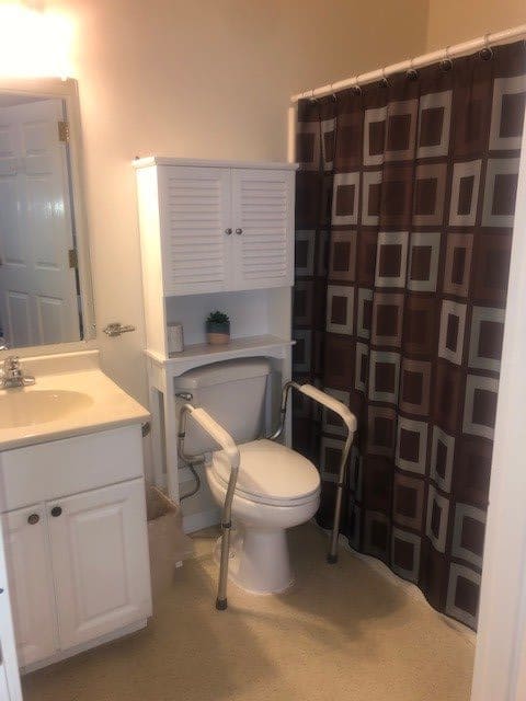 A bathroom with toilet safety rails, a sink, and a patterned shower curtain.