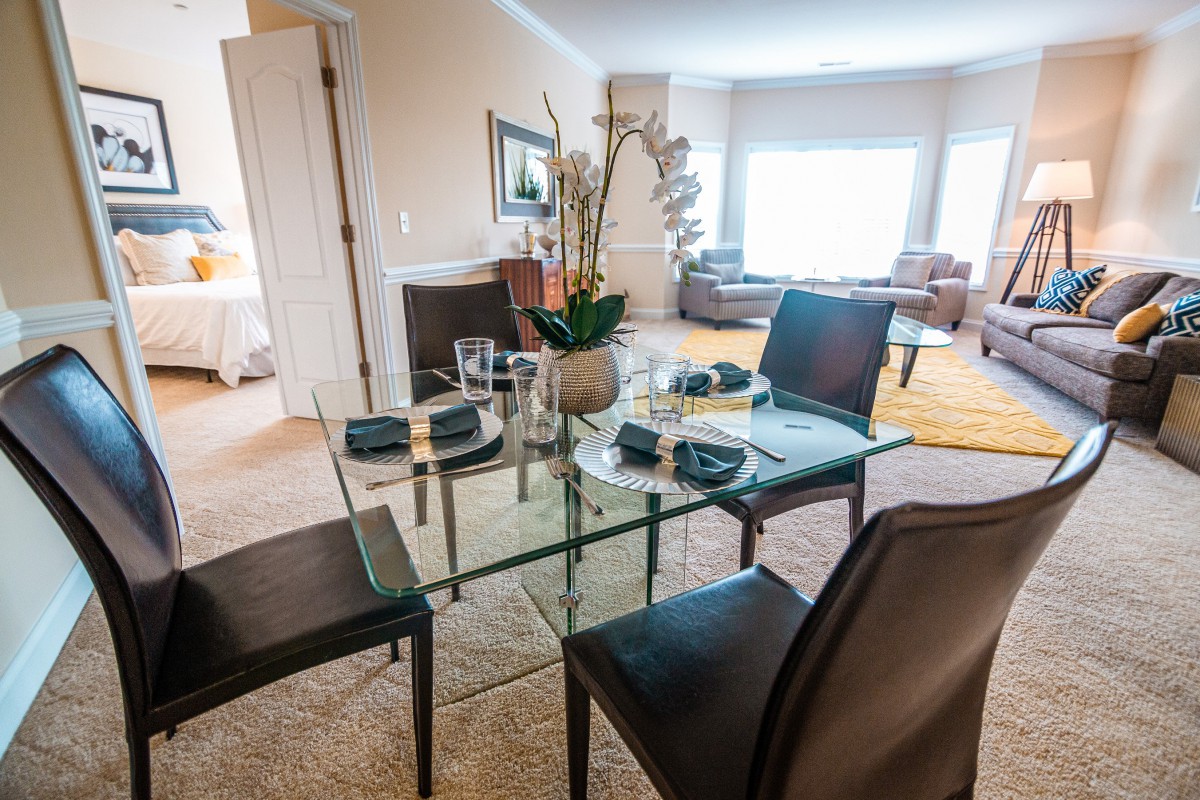 A modern apartment dining area with a glass table set and comfortable living room in view.