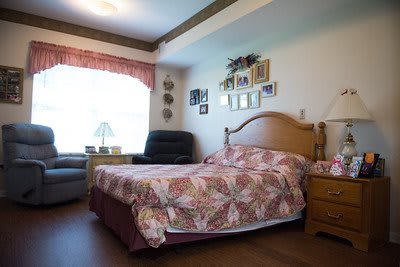 A cozy bedroom with a floral bedspread, armchair, and natural light coming through the window.