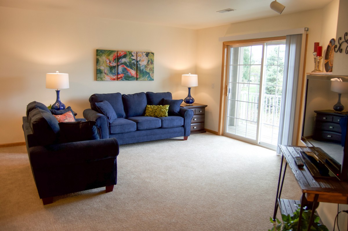 A cozy living room with a blue sofa, two lamps, and sliding glass doors leading to the outside.