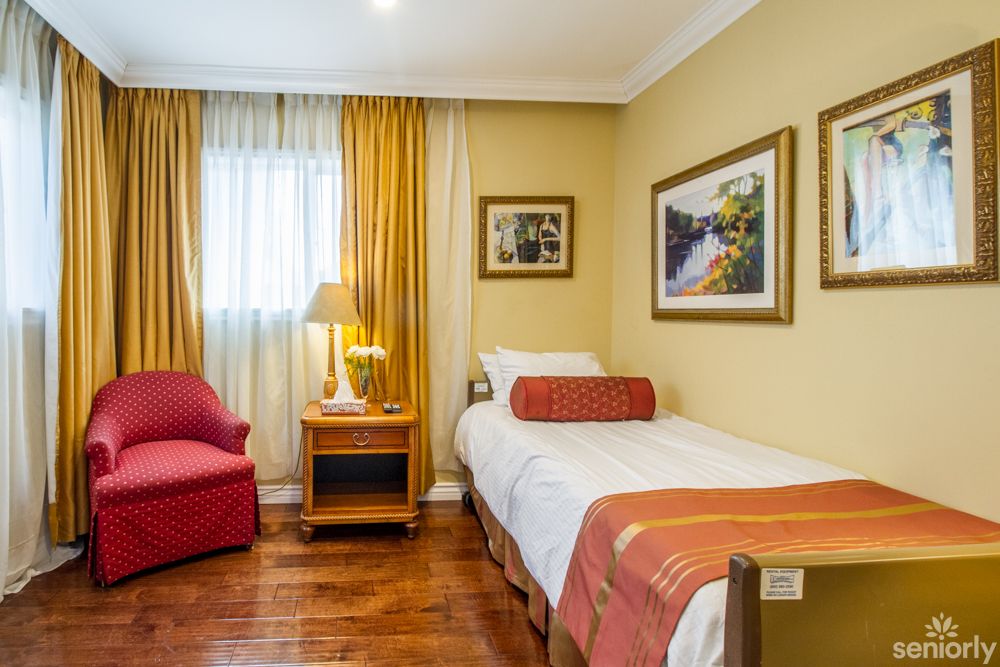 A cozy bedroom with a single bed, red armchair, and warm decor.