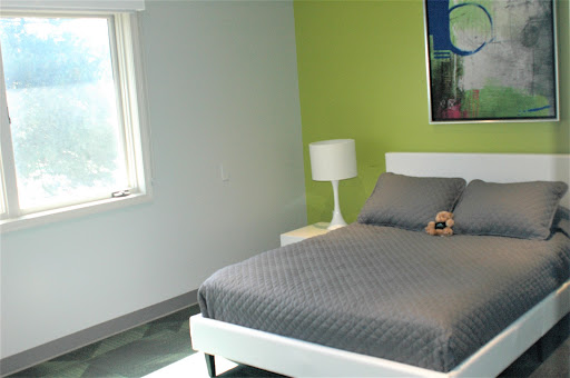 A minimalist bedroom featuring a green accent wall and modern furnishings.