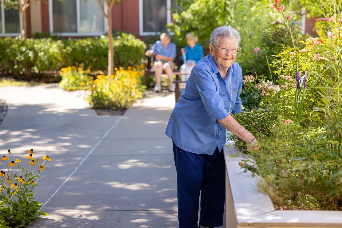 An elderly person tending to a garden in a retirement home setting.