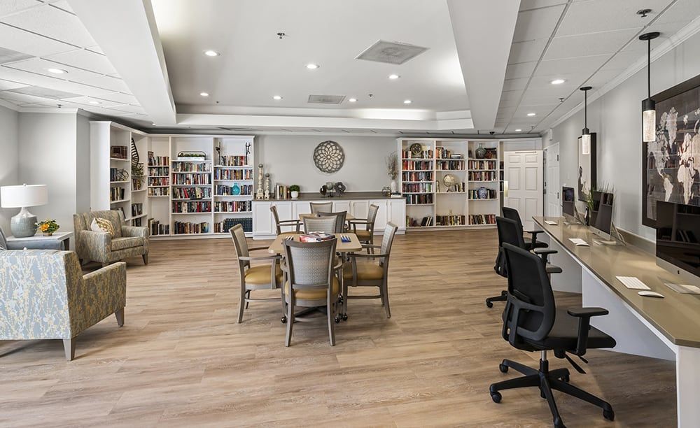 A modern library interior with bookshelves, tables, and chairs arranged on a wooden floor.