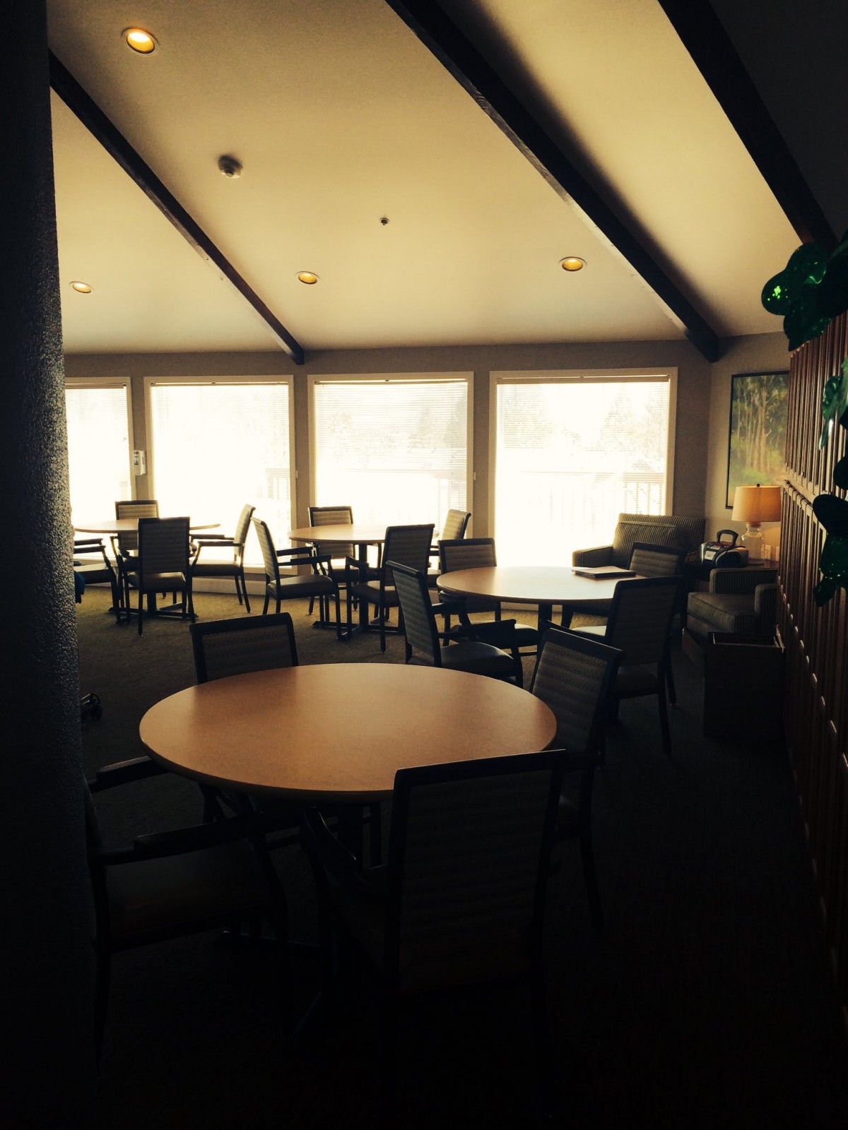 A sunlit room with tables and chairs arranged near large windows.