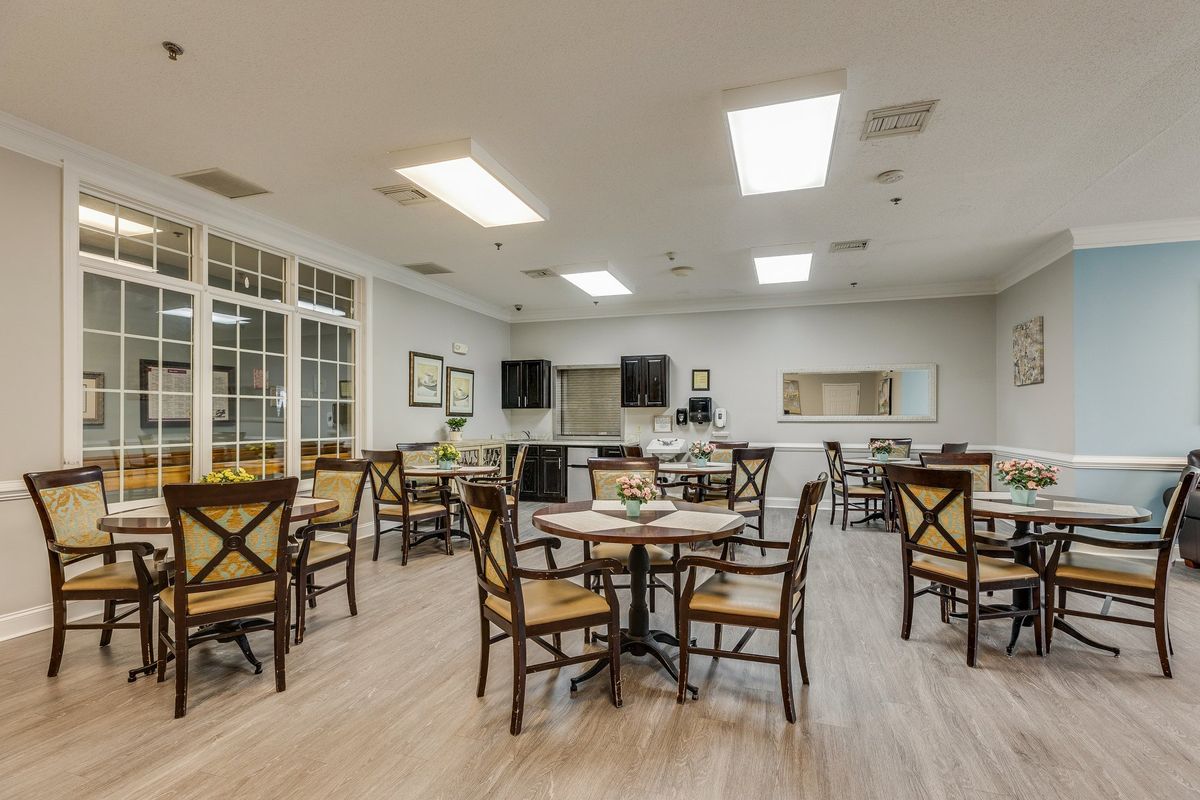A spacious dining area with multiple tables and chairs, featuring bright lighting and a wooden floor.