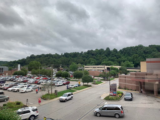 A view of a parking lot at a shopping center, surrounded by lush hills under a cloudy sky.