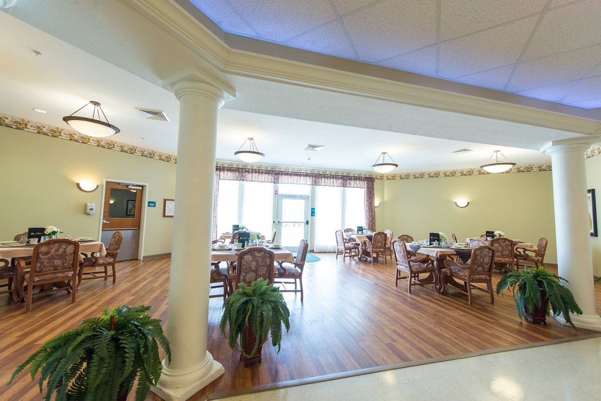 A spacious dining area with tables and chairs arranged neatly, featuring large windows and indoor plants.
