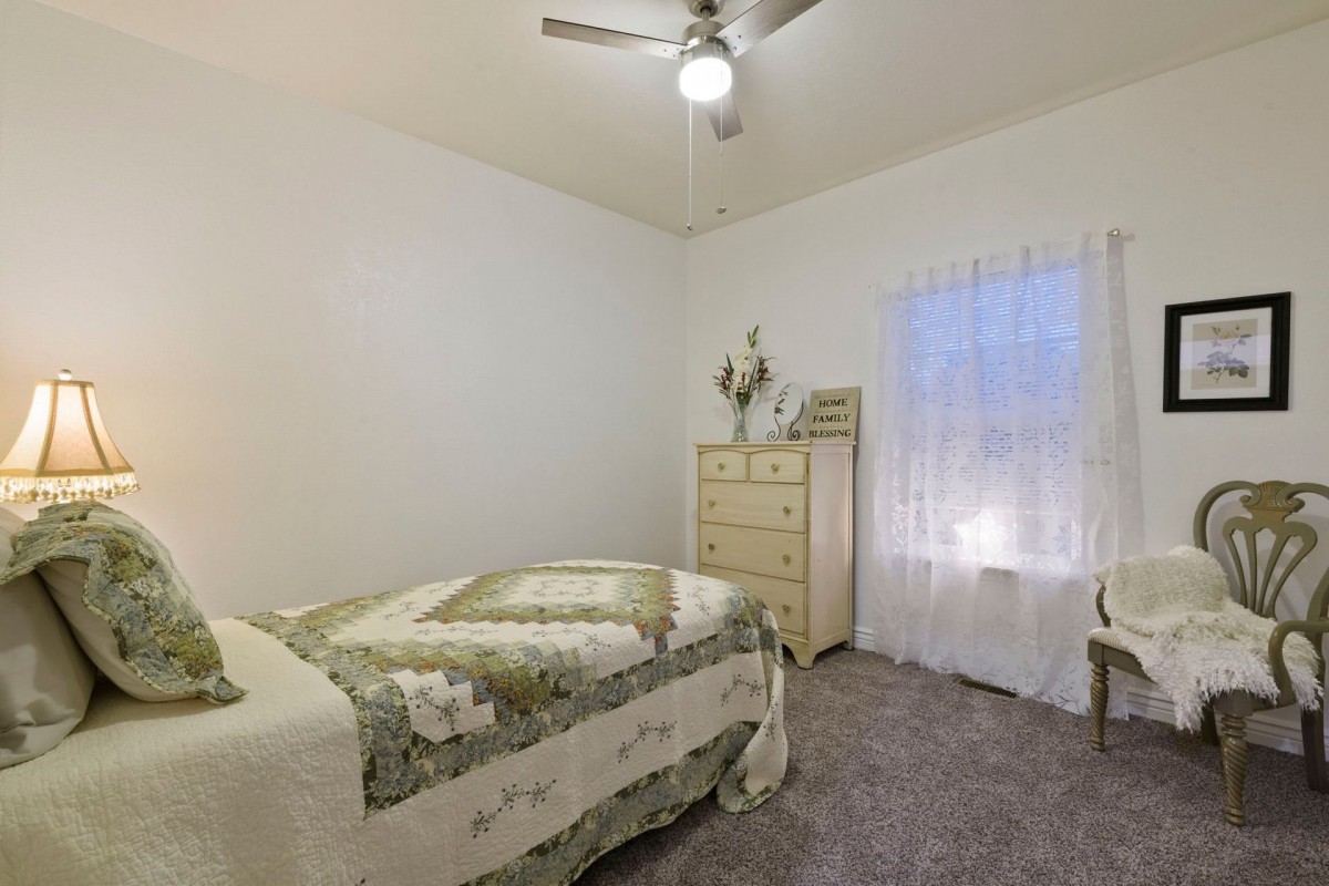 A cozy bedroom featuring a single bed with a patterned quilt, a dresser with decorative items, and a ceiling fan.