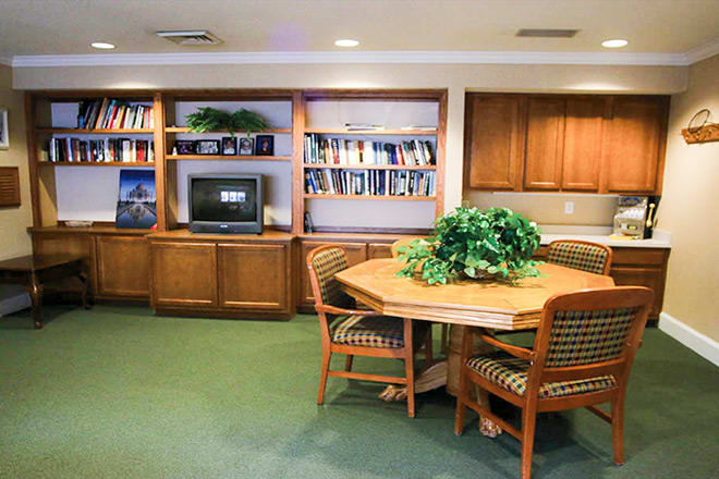 A cozy reading room with a bookshelf, table, and chairs.