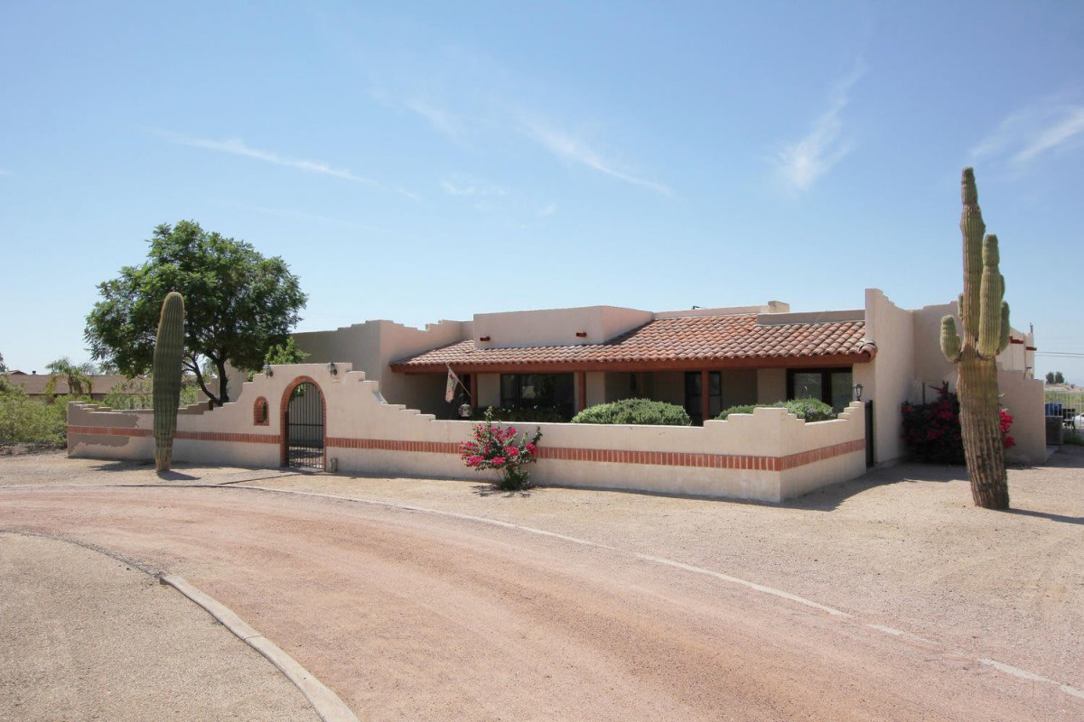 A single-story stucco house with a tile roof set in a desert landscape.