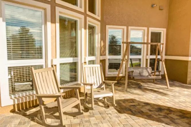 Sunny patio with wooden chairs and a swing, near large windows.