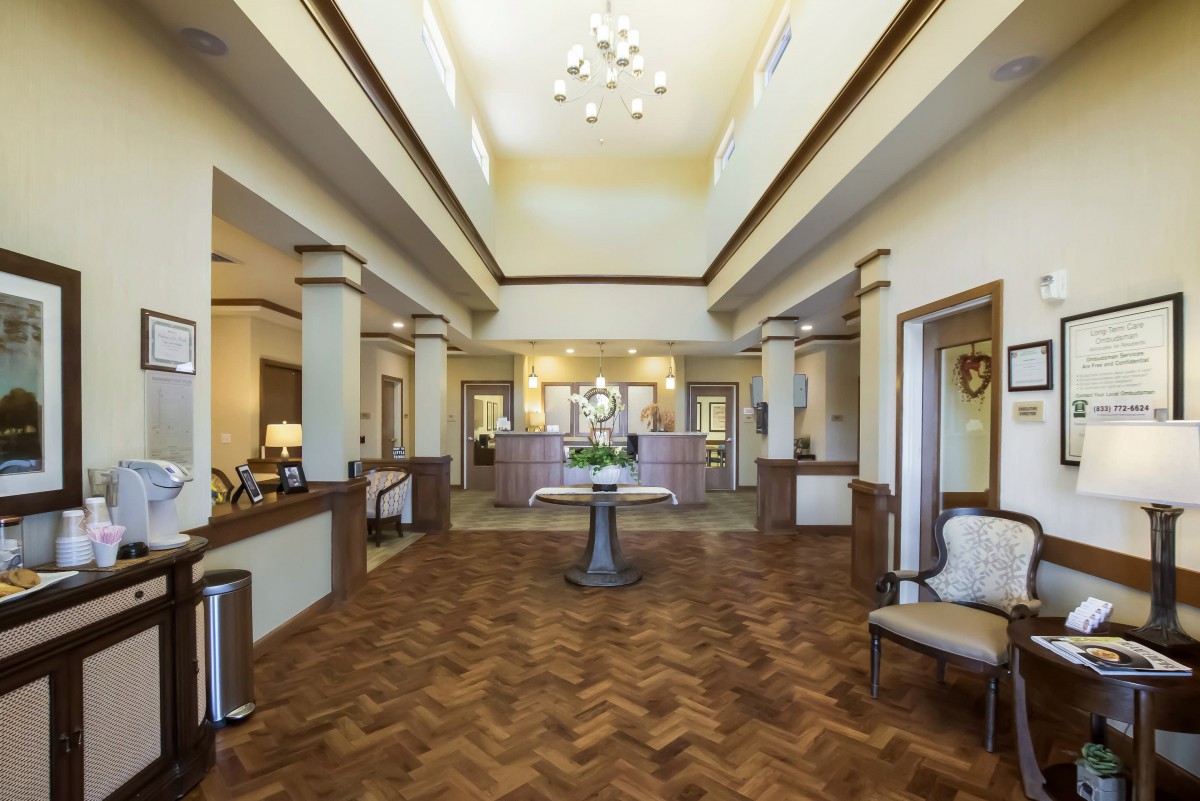 A spacious and elegant lobby with a reception desk, featuring a chandelier, wood flooring, and comfortable seating.