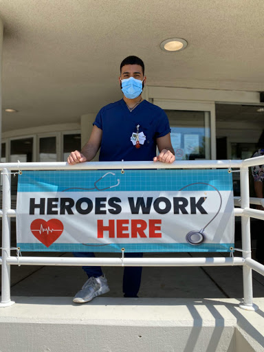 A healthcare worker stands proudly in front of a sign promoting the dedication and hard work of medical professionals.