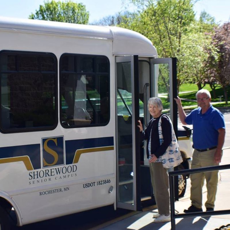 Two people boarding a small bus on a sunny day.