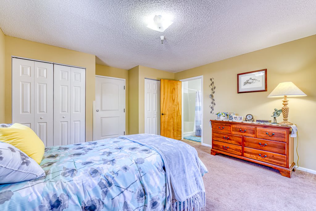A cozy bedroom with neutral walls, featuring a bed and a wooden dresser.