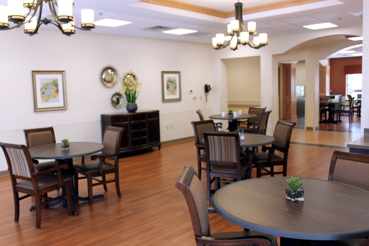 A cozy dining area with round tables and chairs, decorated with artwork and elegant lighting.