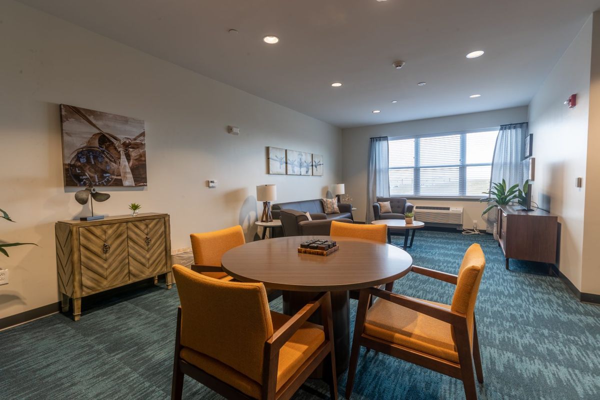 A modern living room featuring a round table with chairs, a comfortable sofa, and large windows allowing natural light.