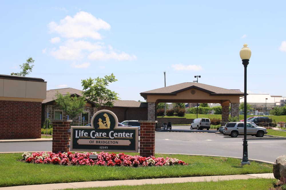 Entrance of a Life Care Center with a sign, landscaping, and parking area.