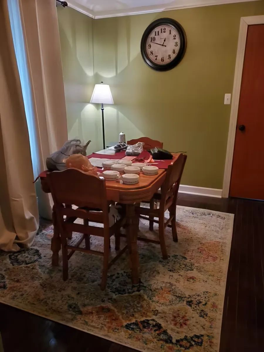A cozy dining area with a wooden table and chairs, set for a meal, illuminated by a standing lamp.