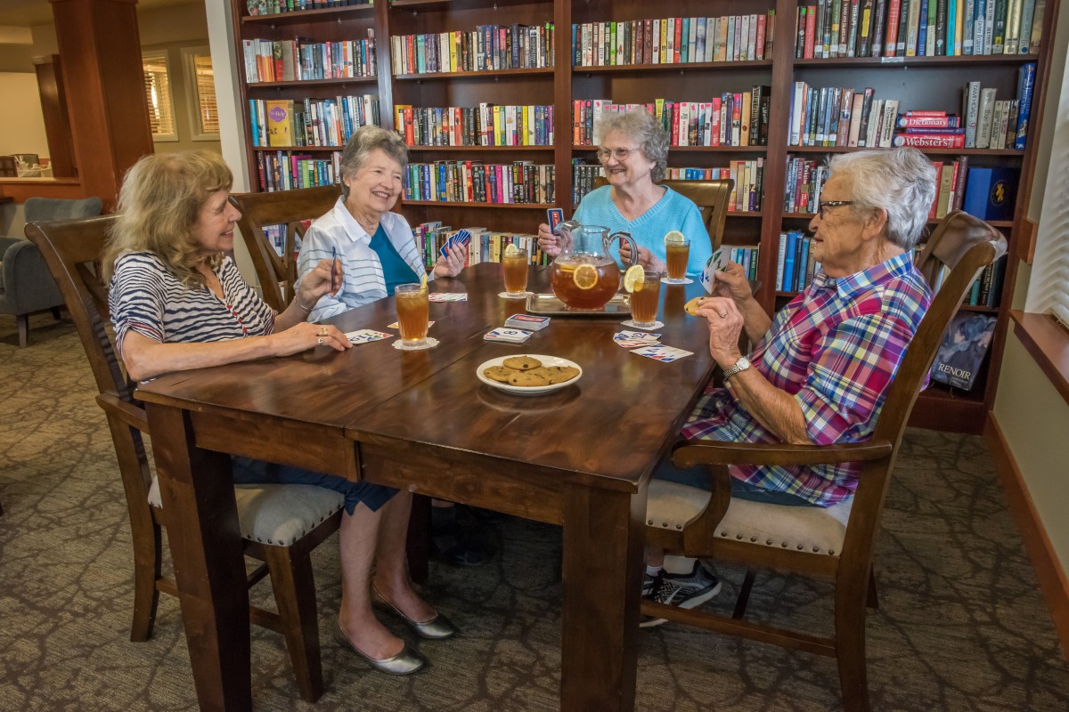 A group of seniors enjoying drinks and conversation in a cozy library setting.