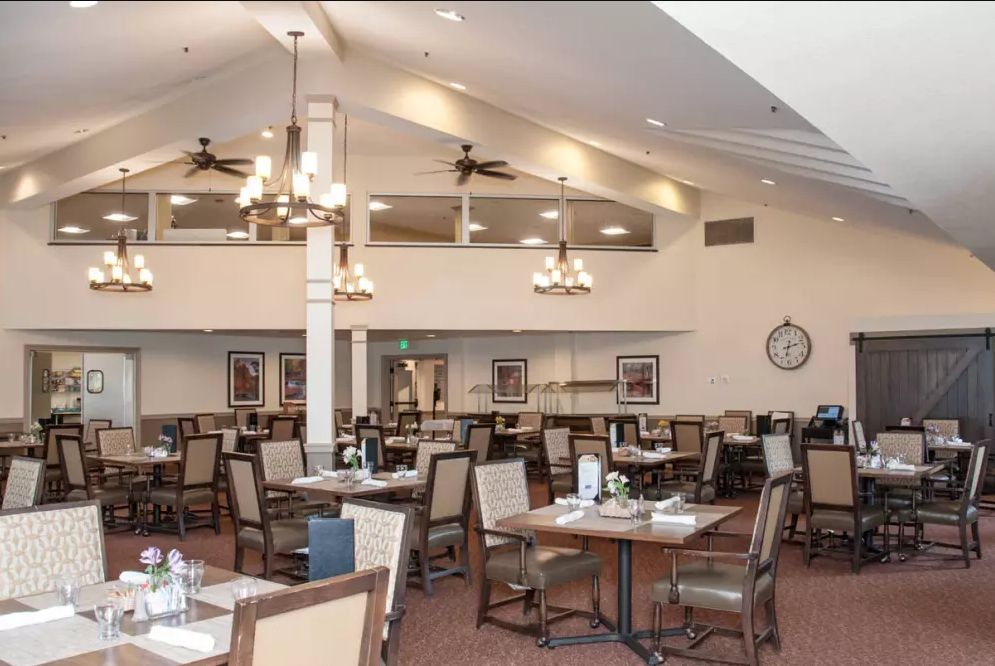 A spacious dining area with numerous tables and chairs, featuring ceiling fans and chandeliers.