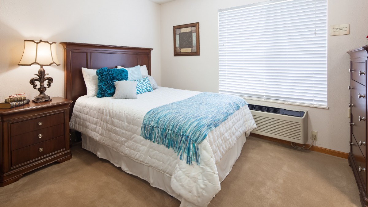 A neatly arranged bedroom featuring a bed with blue and white bedding near a window.
