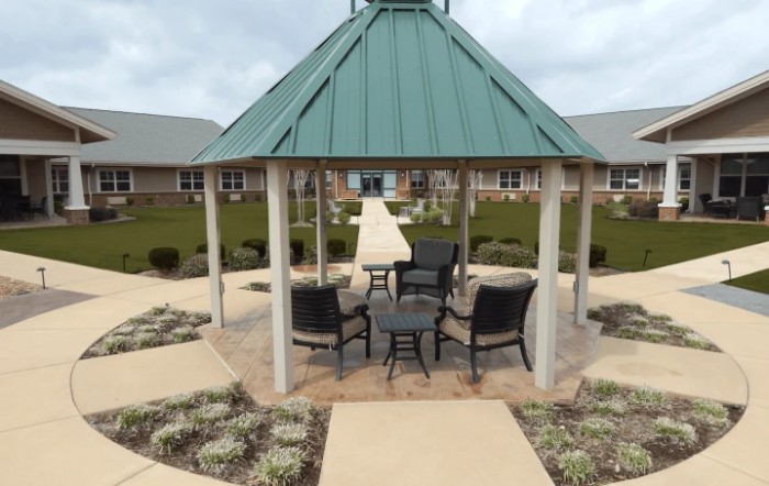 A gazebo surrounded by landscaping with chairs and a table, set beside a pathway.
