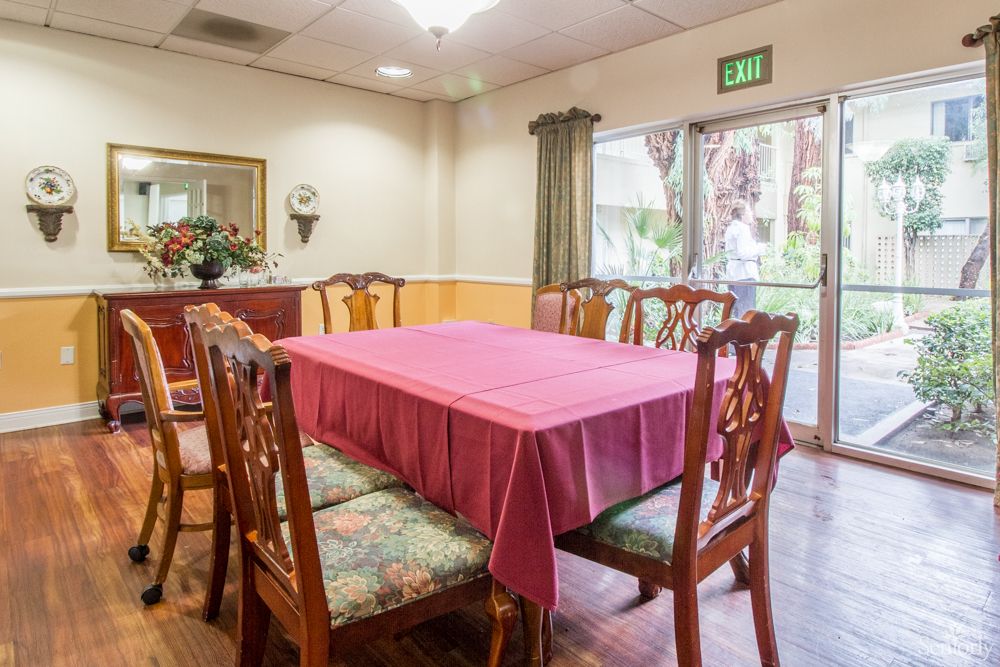 A cozy dining room with a pink tablecloth on the table and wooden chairs around it.