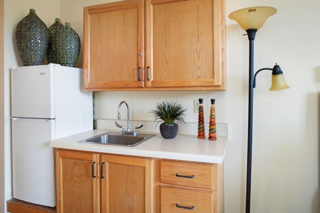 A compact kitchen area featuring wooden cabinets, a small sink, decorative items, and a floor lamp.