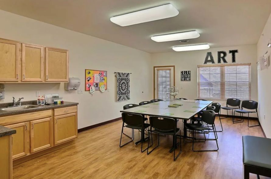 A well-lit art room with tables and chairs arranged for group activities, featuring colorful artwork on the walls.