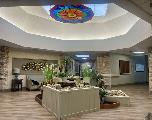 A serene and modern lobby featuring a stained glass ceiling, lush plants, and a calming water feature.