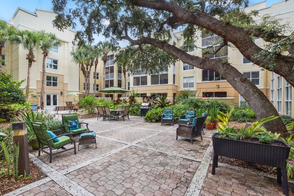 A serene courtyard with outdoor seating surrounded by lush greenery and apartment buildings.