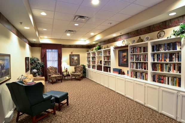 A cozy library room featuring wall-to-wall bookshelves, comfortable seating, and a warm atmosphere.