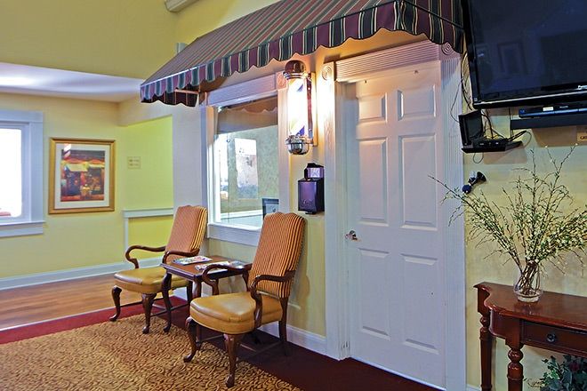 A cozy interior space with a waiting area featuring two chairs, a small table, an awning above a window, and a door.