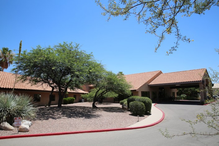 A building with a desert landscape, featuring trees and a driveway.