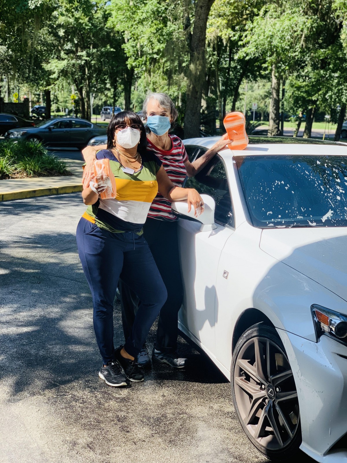 Two people wearing masks standing next to a car outdoors.