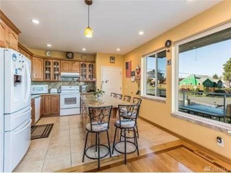 A cozy kitchen with wooden cabinets, a central island with bar stools, and a large window offering ample natural light.
