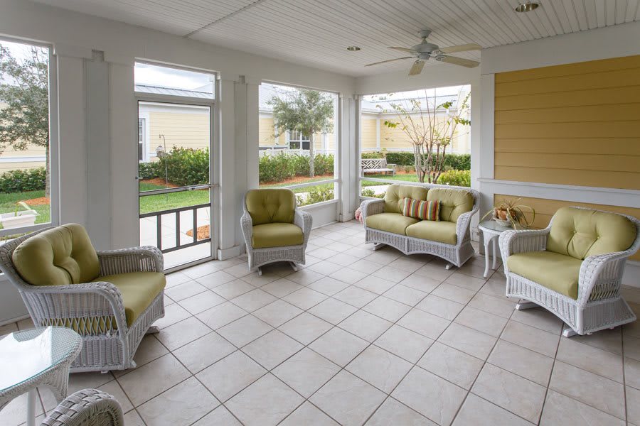 A bright sunroom featuring wicker furniture with green cushions and a tiled floor.