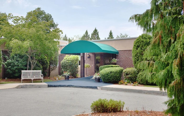 A building entrance with a green awning, surrounded by well-maintained landscaping.