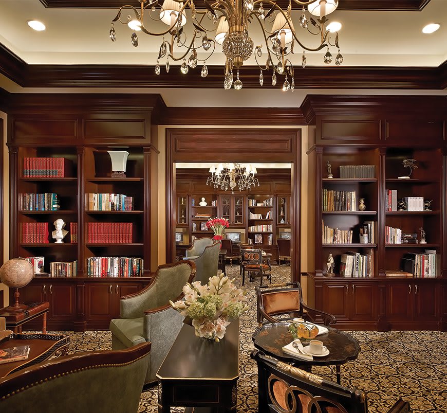 A luxurious library interior with wooden bookshelves, elegant furniture, and a chandelier.