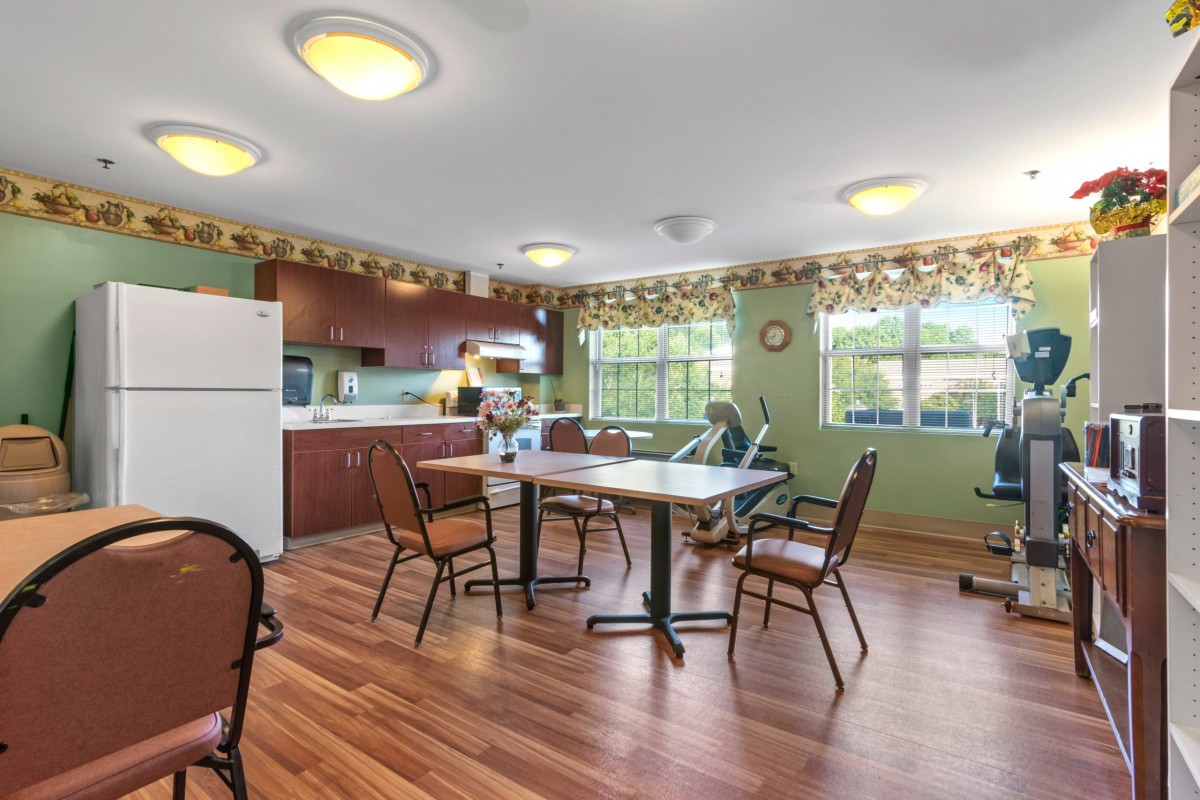 A spacious kitchen and dining area with wooden flooring, featuring a table and chairs, and large windows allowing natural light.