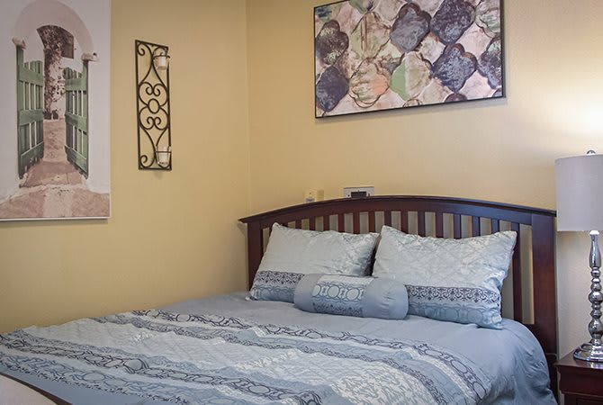 A cozy bedroom with a neatly made bed, featuring decorative pillows and artwork on the wall.